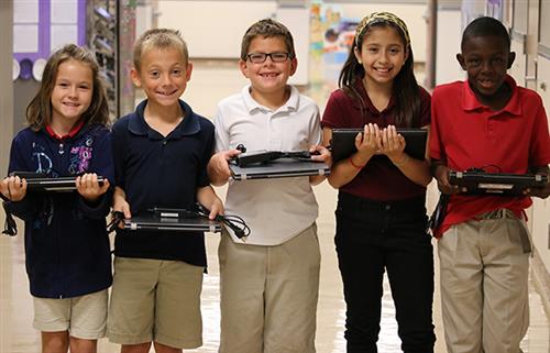 five students holding their chromebook and smiling 